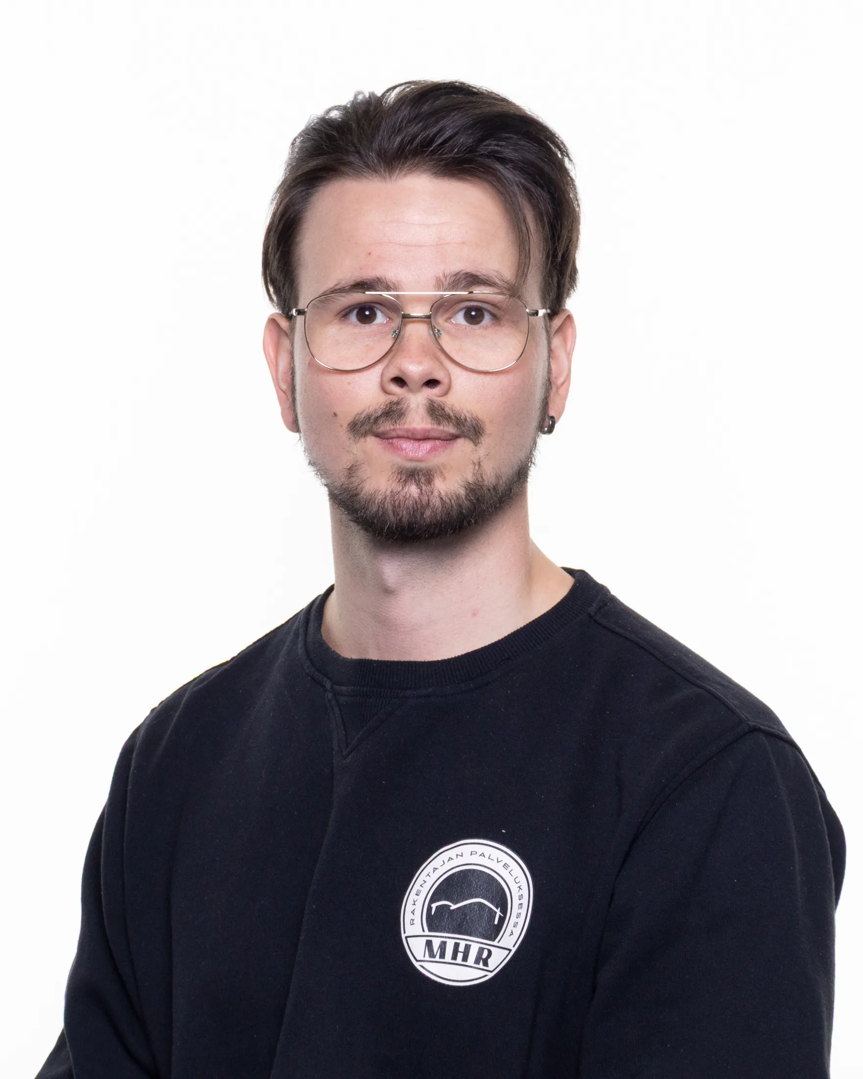 Muotokuva nuoresta miehestä silmälaseissa, mustassa paidassa, jossa on MHR-logo, valkoisella taustalla.